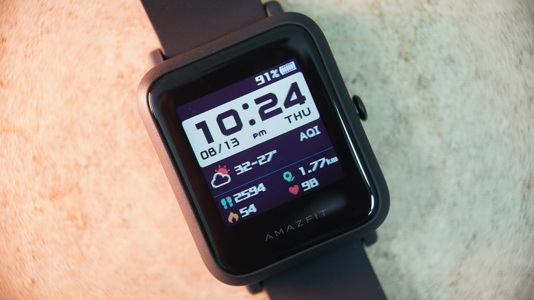 An Amazfit Bip S displaying the time, weather, and health information as it sits against a flat surface