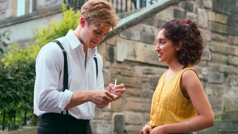 Leo Woodall as Dexter writing on piece of paper next to Ambika Mod as Emma in One Day