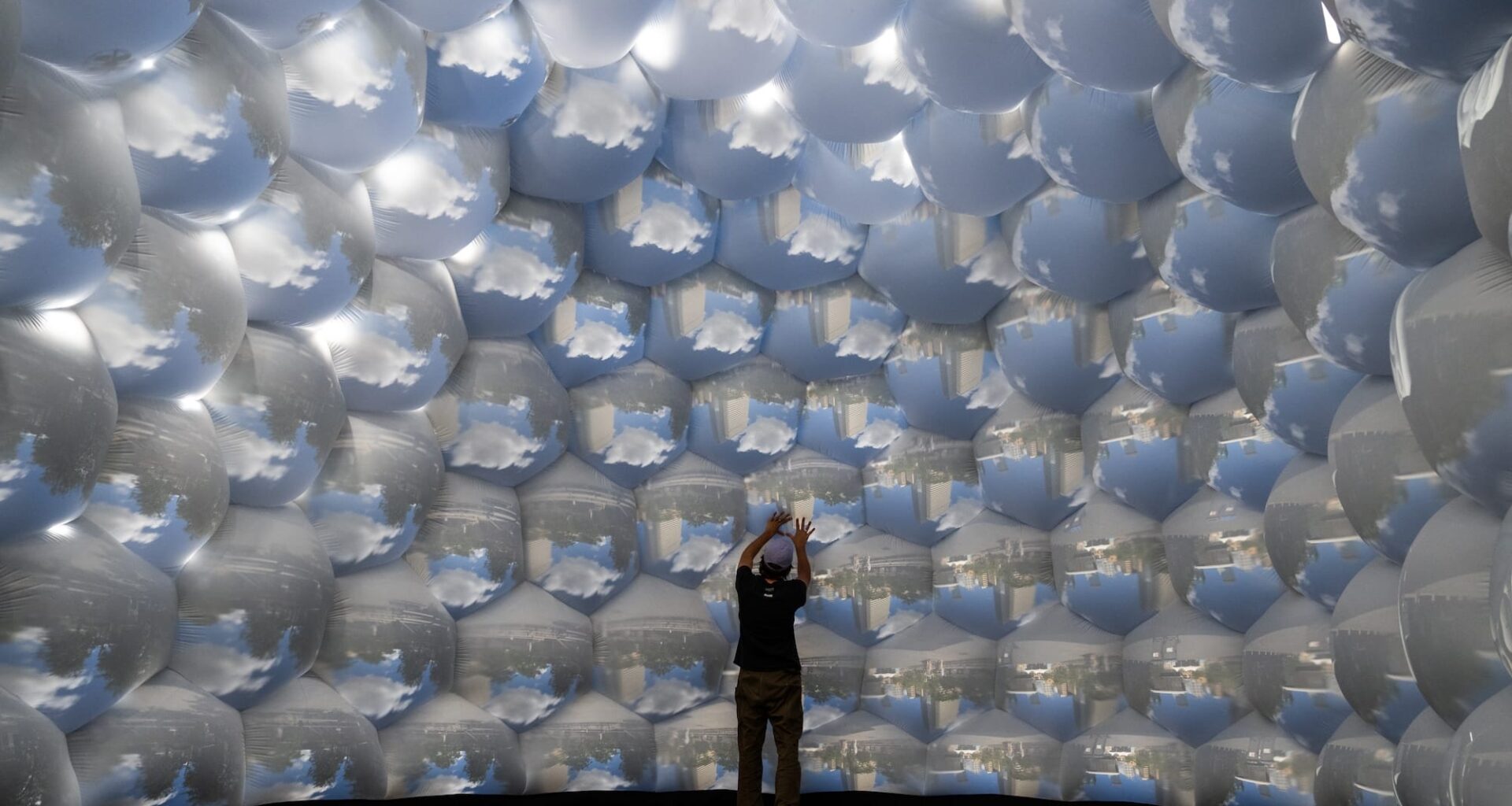 the interior of an architectural, inflatable compound camera installation with a person standing inside it, looking up at bubble-like forms featuring images of outside captured by tiny apertures