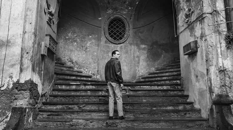 Tom Ripley looking nervously over his shoulder while standing on a set of massive stone steps
