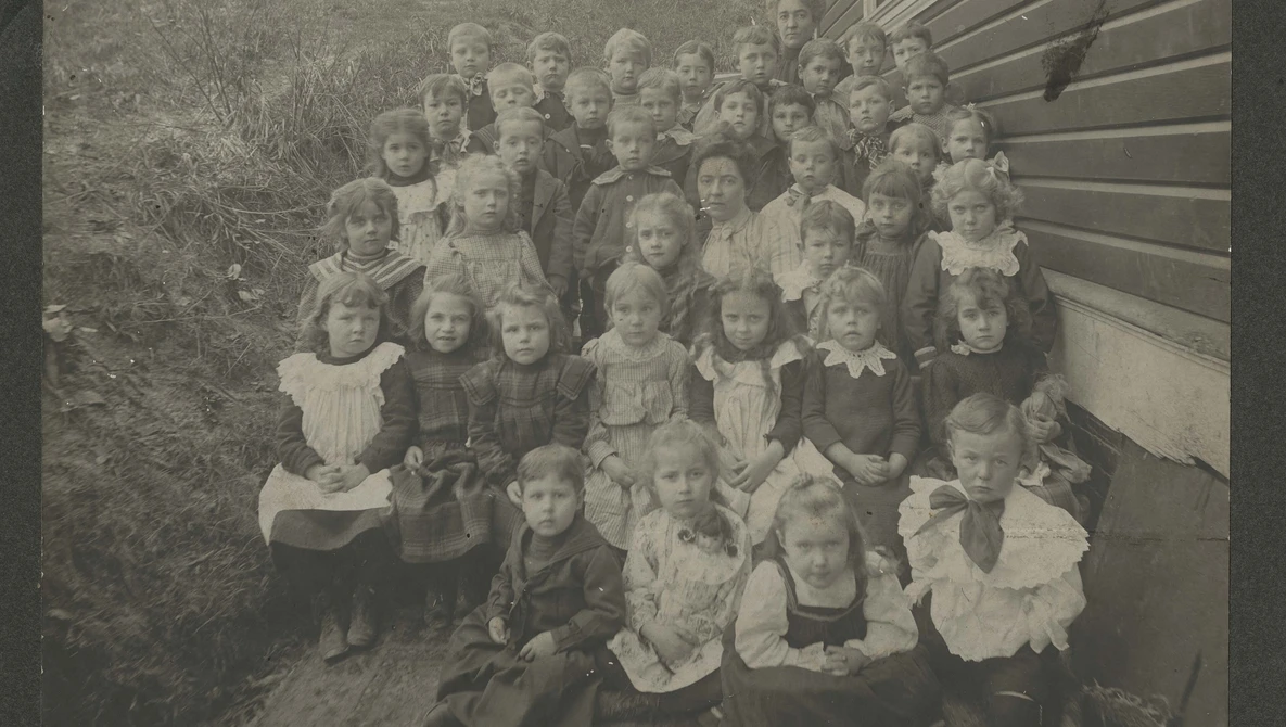 Large group portrait of approximately 40 children arranged in rows outside a building