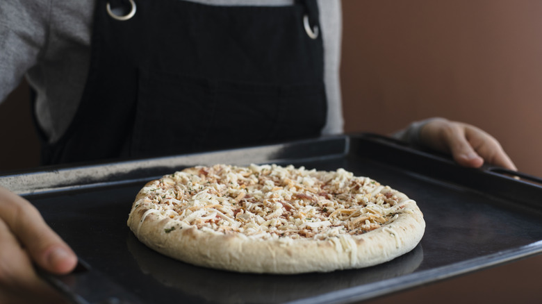 A frozen pizza on a baking sheet being carried to the oven