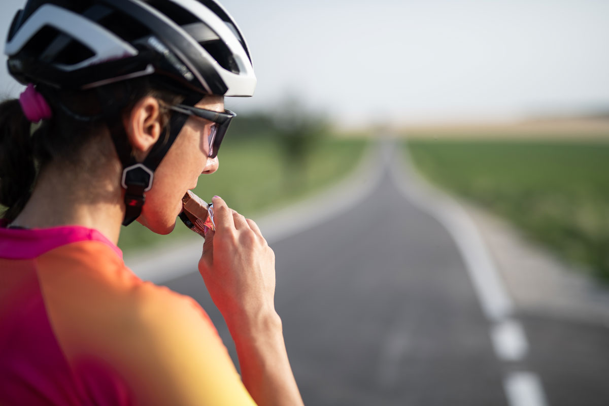 Close-up of female road cyclist eating a protein bar for recovery after cycling exercise.