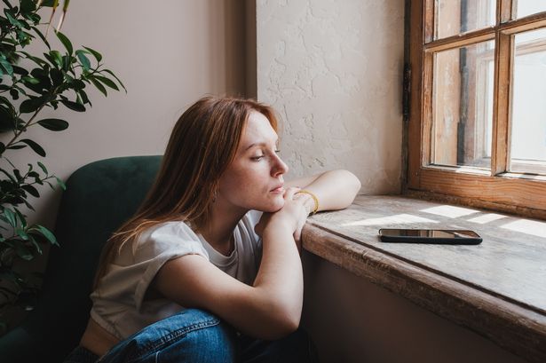 Upset redhead teen girl sitting by window