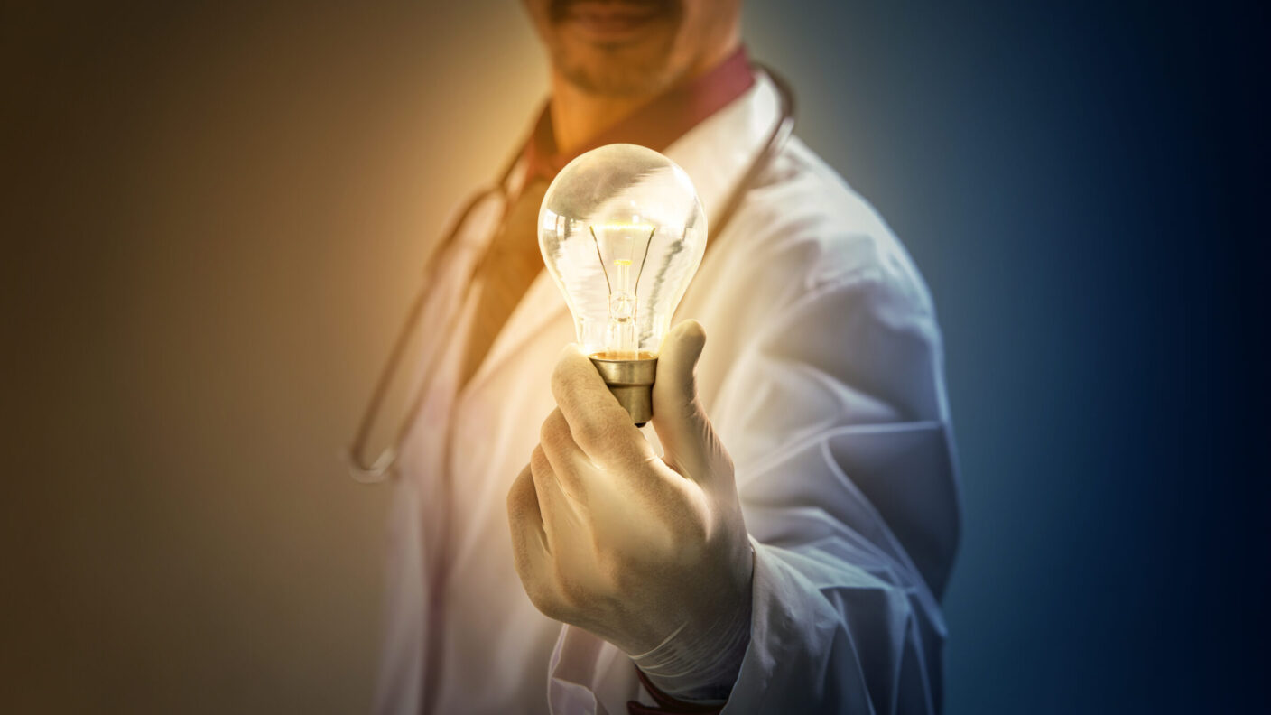 A photo of a man with a stethoscope and doctor's coat holding an illuminated light bulb.