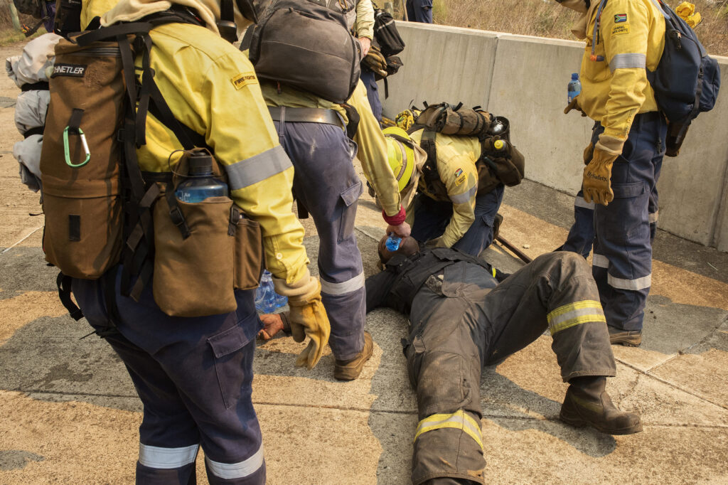 Firefighters try to revive a colleague who collapsed due to the smoke and heat as a forest fire burns above the University of Cape Town in South Africa on April 18, 2021. Credit: Rodger Bosch/AFP via Getty Images