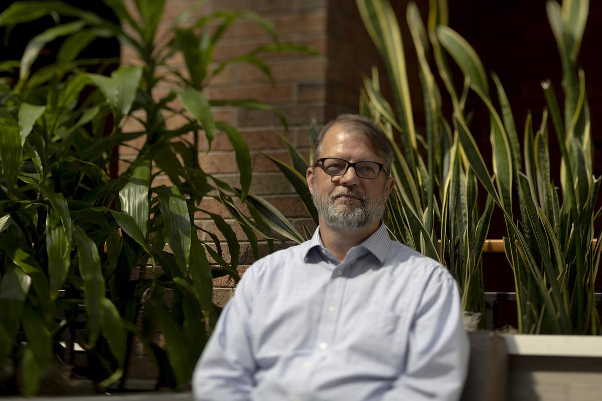 Mark Sander poses for a portrait in an office building among plants