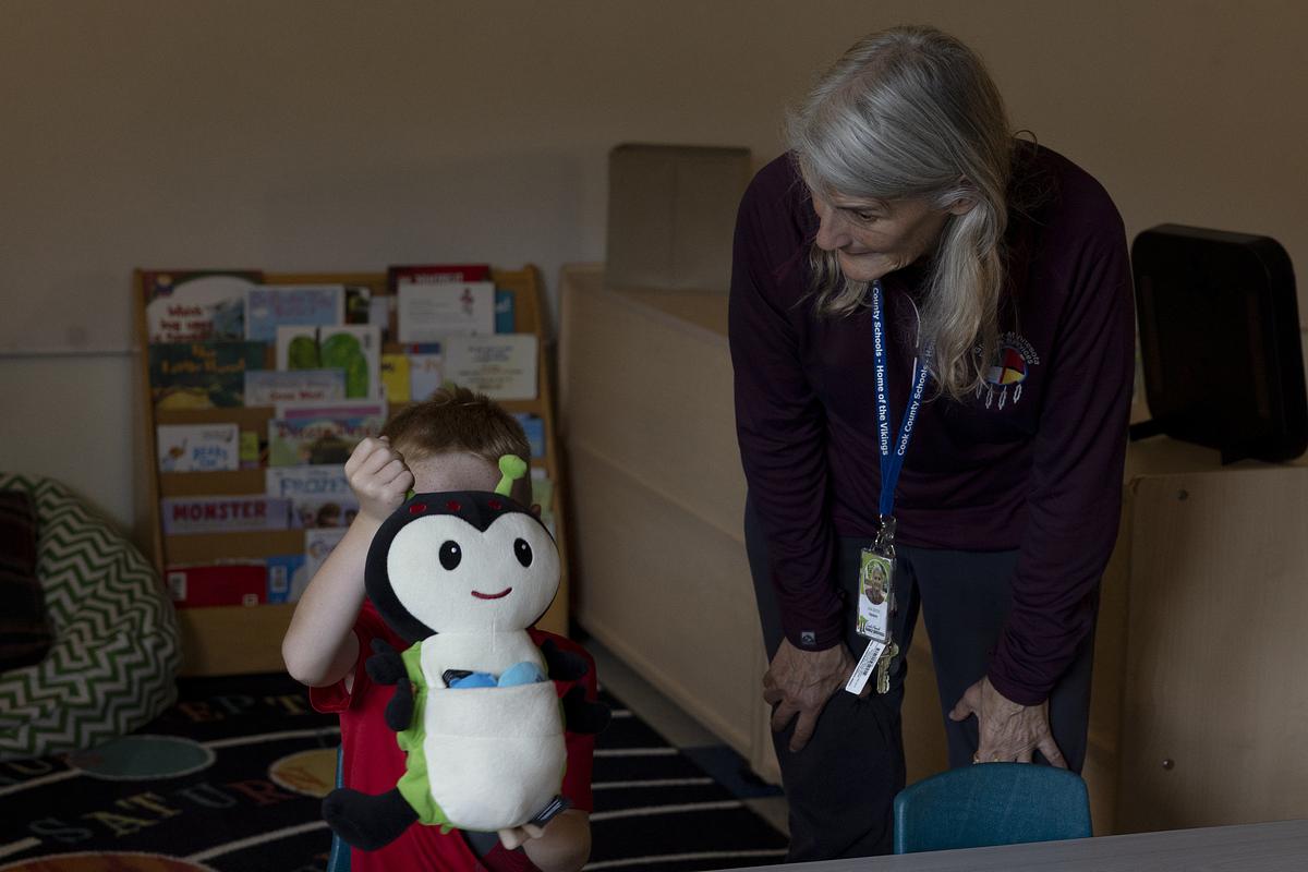 Lisa Sater talks to a boy in his preschool classroom while a stuffed toy obscures his identity