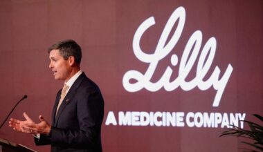 Dave Ricks speaks at a podium in front of a screen displaying the Lilly logo and slogan