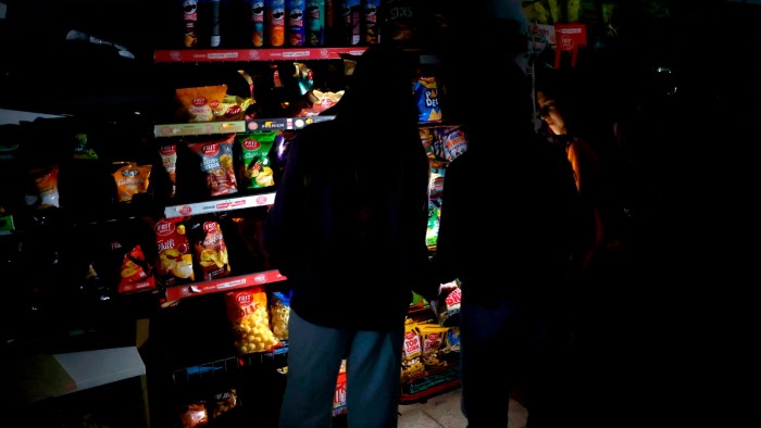 Customers use mobile phone flashlights to browse shelves in a dark supermarket during a power outage in Barcelona, Spain on April 28, 2025.