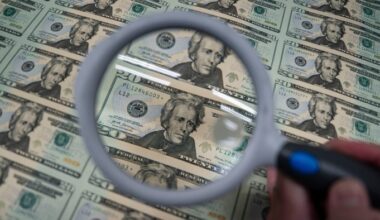 A worker inspects a sheet of uncut $20 bills with a magnifying glass at the US Bureau of Engraving and Printing.