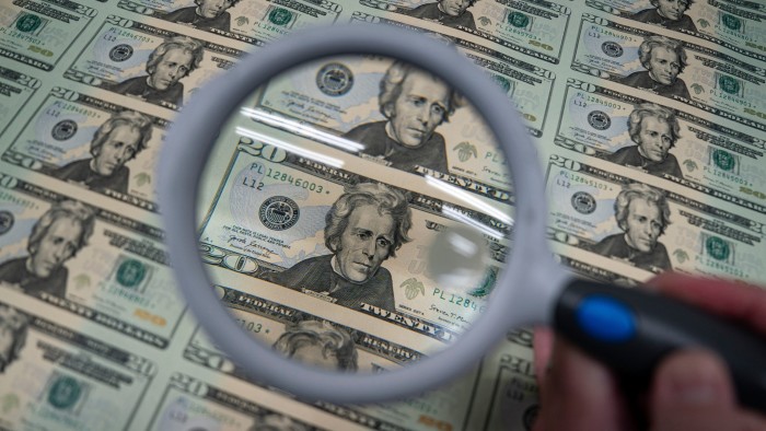 A worker inspects a sheet of uncut $20 bills with a magnifying glass at the US Bureau of Engraving and Printing.