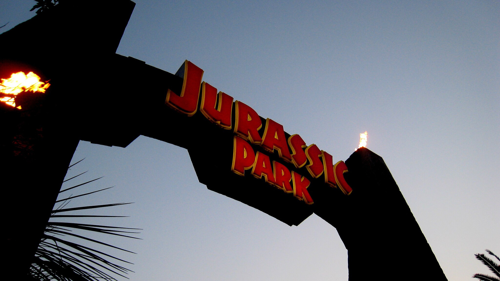 An arch with fiery torches reads "Jurassic Park" in red lettering