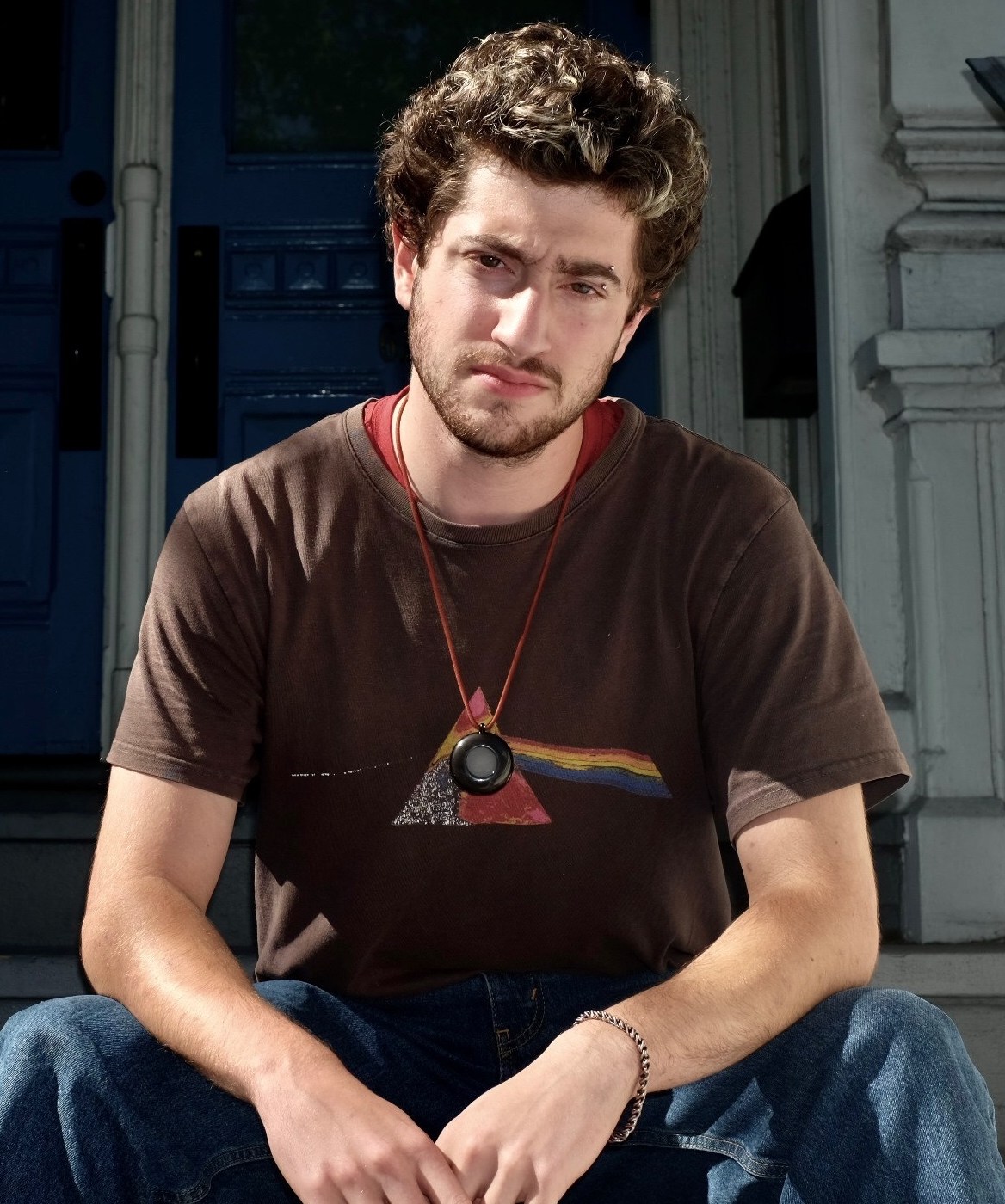 Avi Schiffmann, founder of the AI company FRIEND, sitting on steps in front of a blue door.