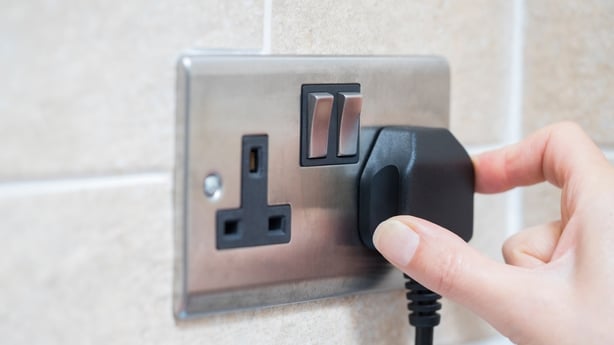 A hand inserts a plug into a socket on a wall.