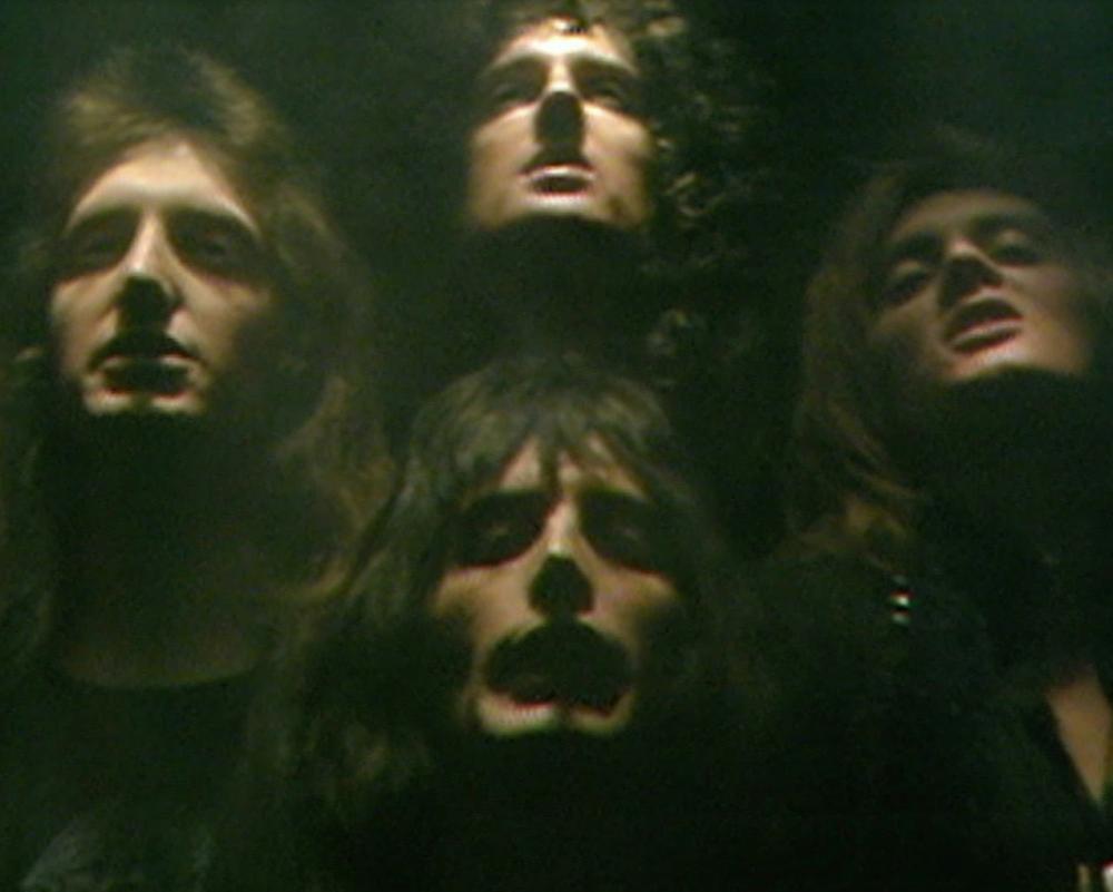 A still from Queen's Bohemian Rhapsody video, showing the four band members' faces against a black background.