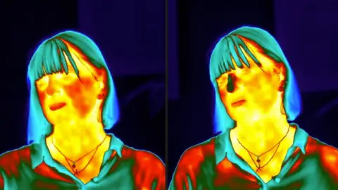 Kevin Church/BBC The picture shows two thermal images - side by side - of the same woman. In the thermal image on the left, her face looks yellow and red, indicating warmth. In the thermal image on the right, her nose is blue. It has cooled down as she has been stressed by the task she is being asked to complete. 