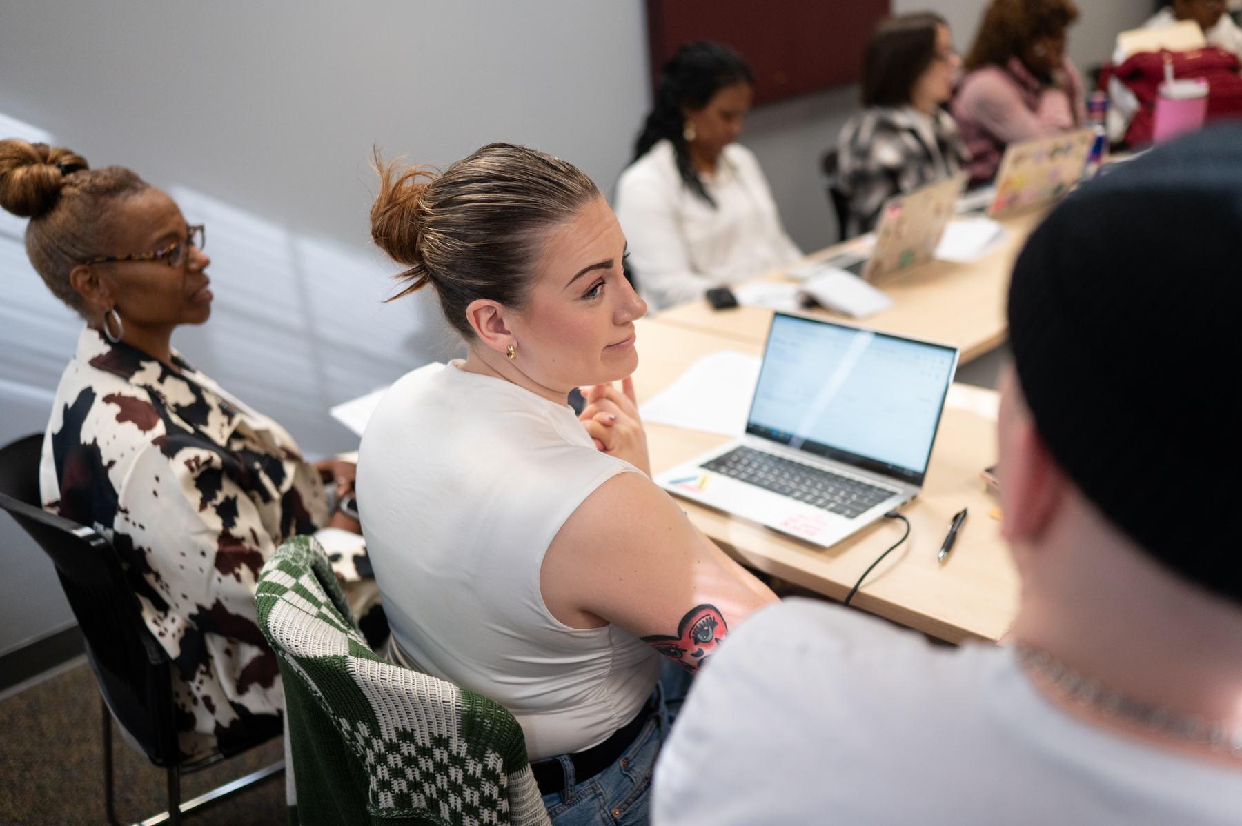 Several people sit around a table with laptops and papers, engaged in discussion in a brightly lit meeting room.