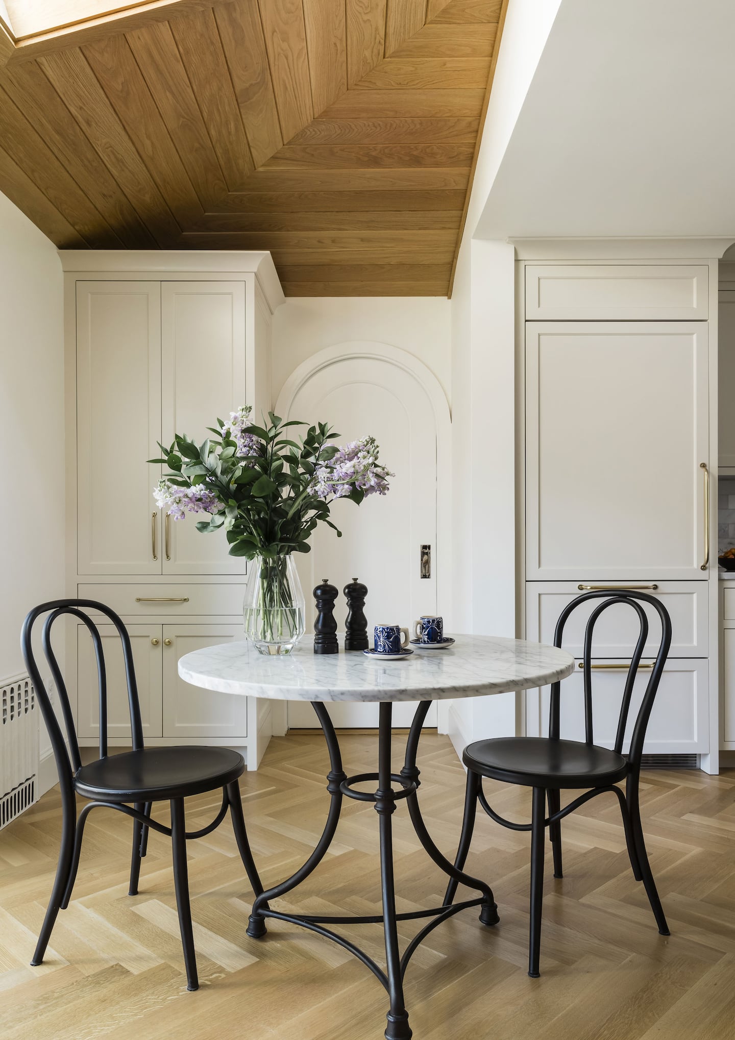 A small round bistro table with white table top and two black chairs. Set in corner of room with wood flooring.
