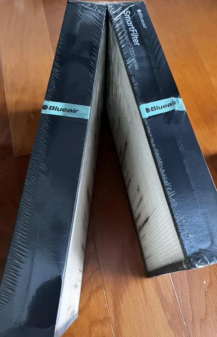 Two Blueair SmartFilter air purifier filters in packaging, standing upright on a wooden floor