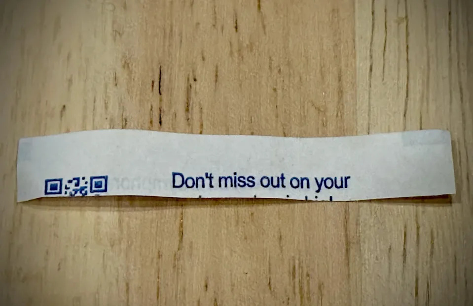 A fortune cookie strip on a wooden table reads, "Don't miss out on your." The sentence is incomplete