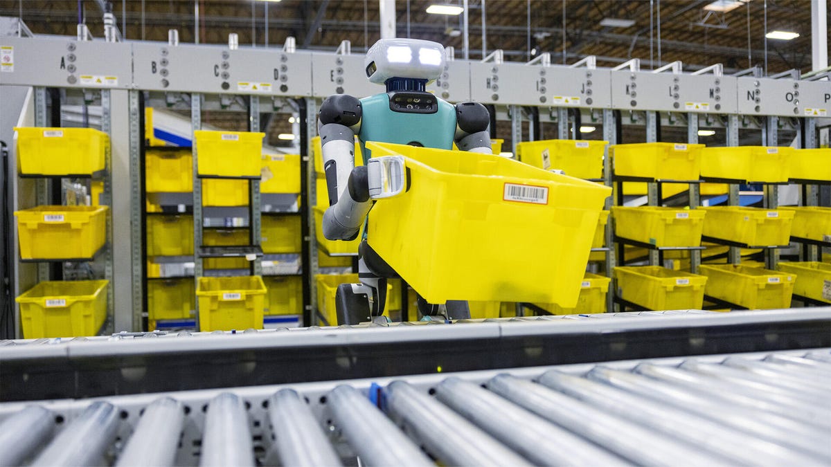 A humanoid robot lifting a yellow bin in a warehouse