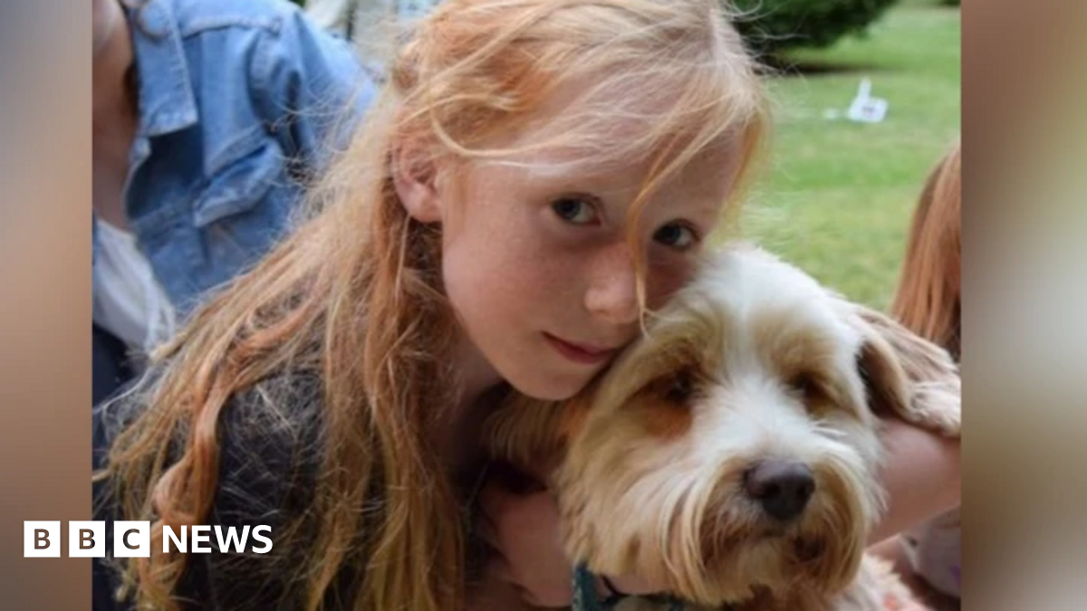 A picture of Ruth Szymankiewicz, who has long ginger hair, cuddling a terrier dog.