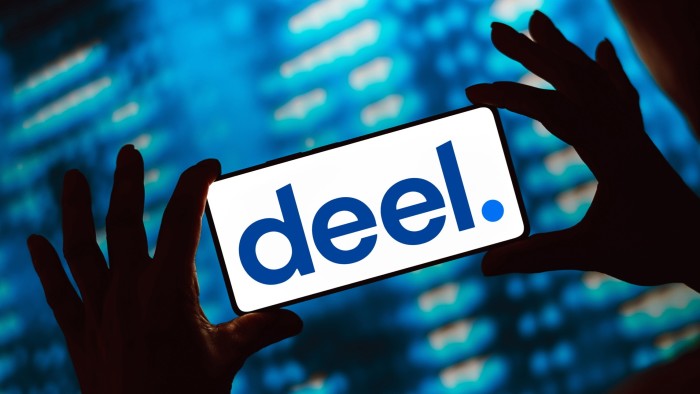 The Deel logo is shown on a smartphone screen held by silhouetted hands against a blue background.