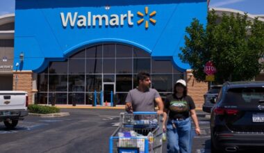 Shoppers exit a Walmart store in Los Angeles, with one person pushing a shopping cart in the parking lot.