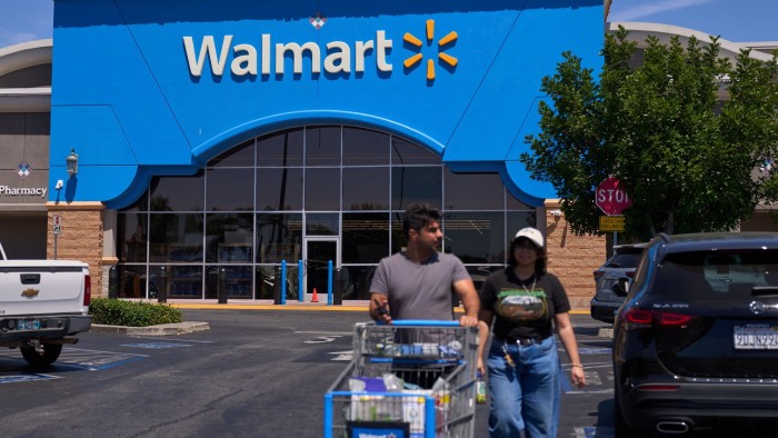 Shoppers exit a Walmart store in Los Angeles, with one person pushing a shopping cart in the parking lot.