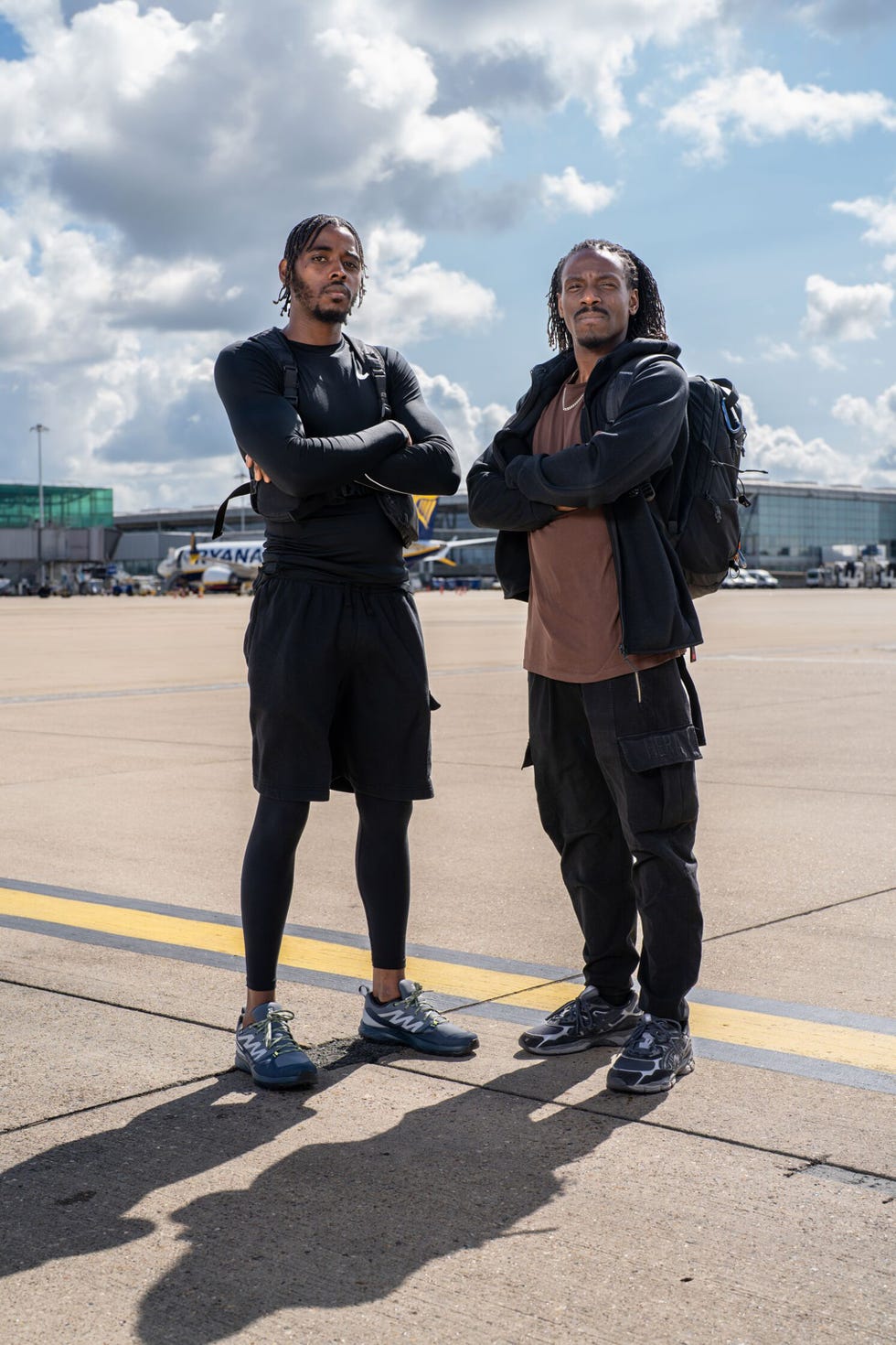 two individuals standing on an airport tarmac with arms crossed