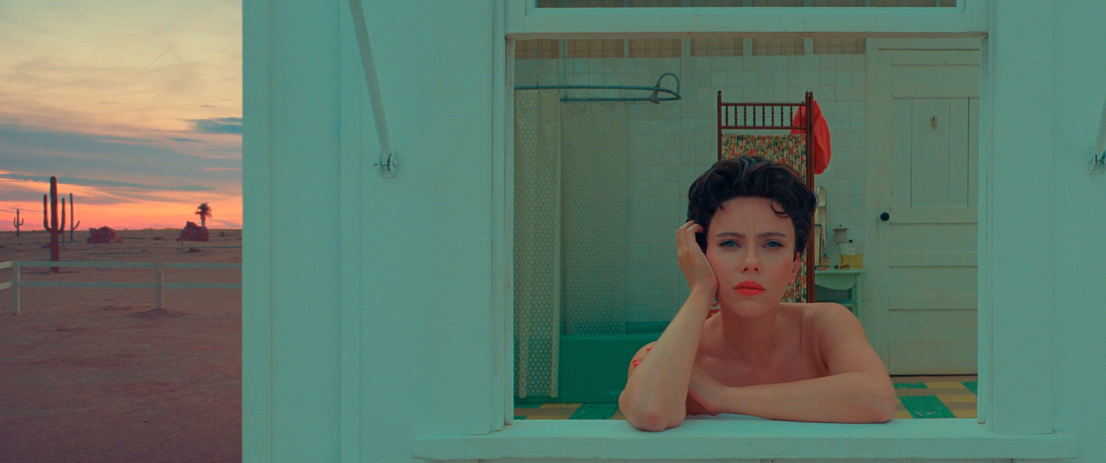 Scarlett Johansson in Asteroid City looking out from a window with a desert landscape behind her.