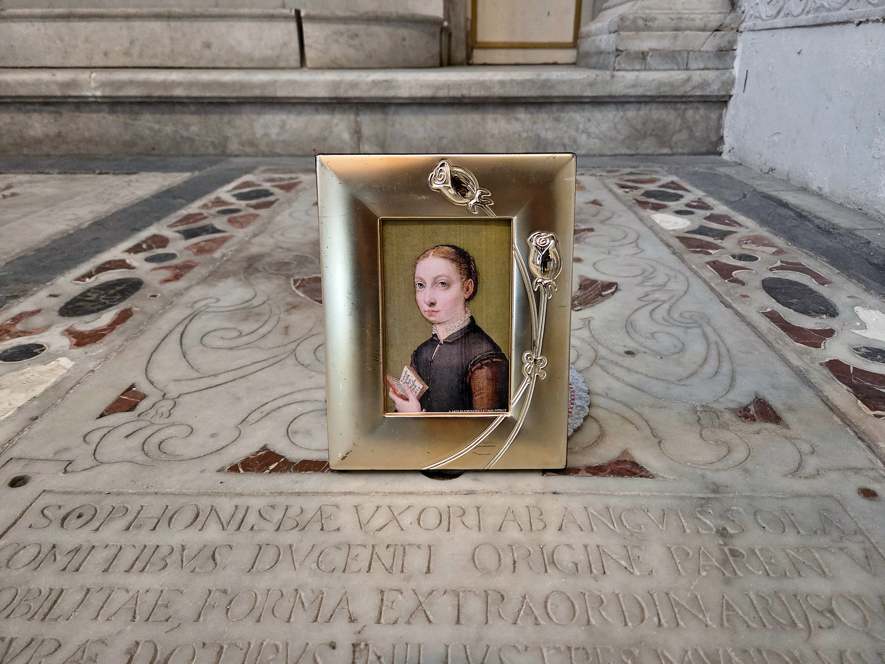 A framed portrait of Sofonisba Anguissola placed on her tomb, which is engraved with her name.