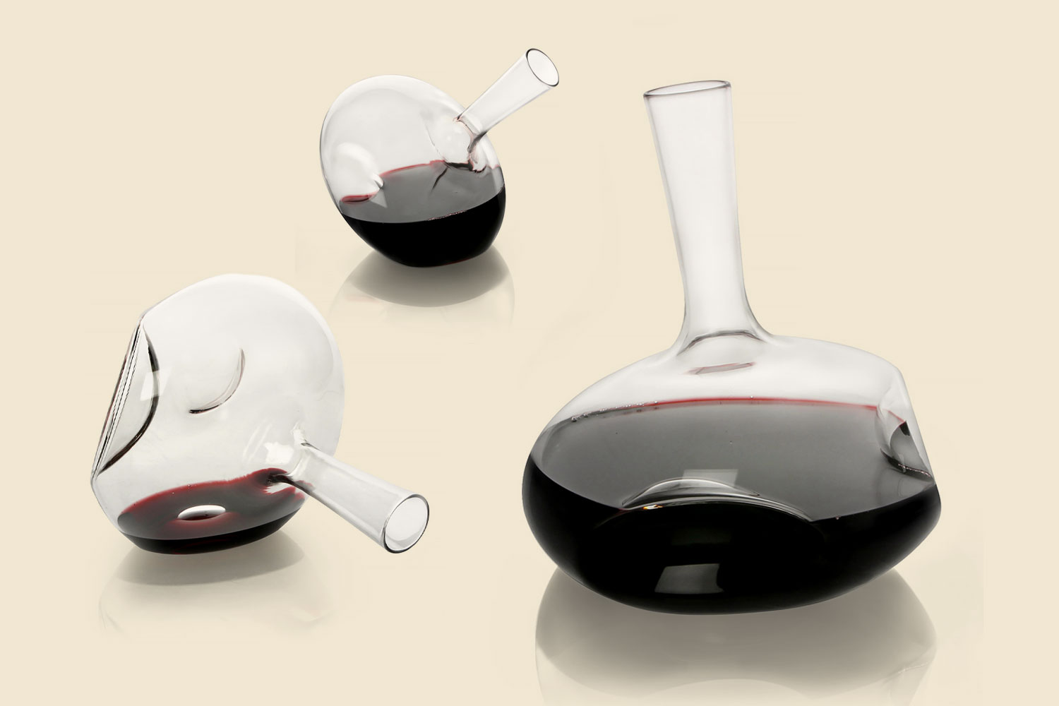 Three decanters, two smaller ones tilted to the left and right, and a larger one standing upright, all partially filled with red wine.
