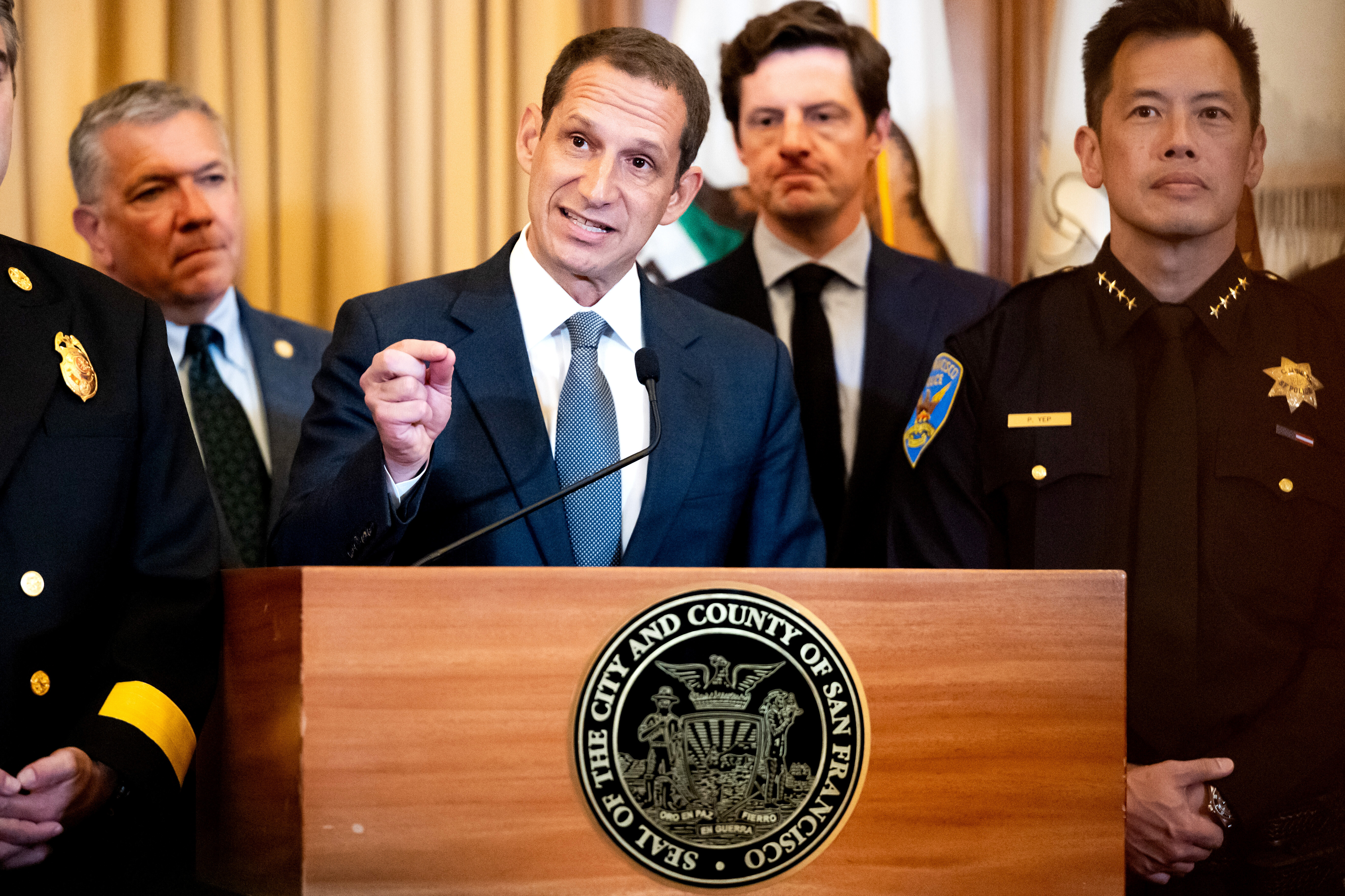 San Francisco Mayor Daniel Lurie speaking at a podium with city leaders and law enforcement officials.