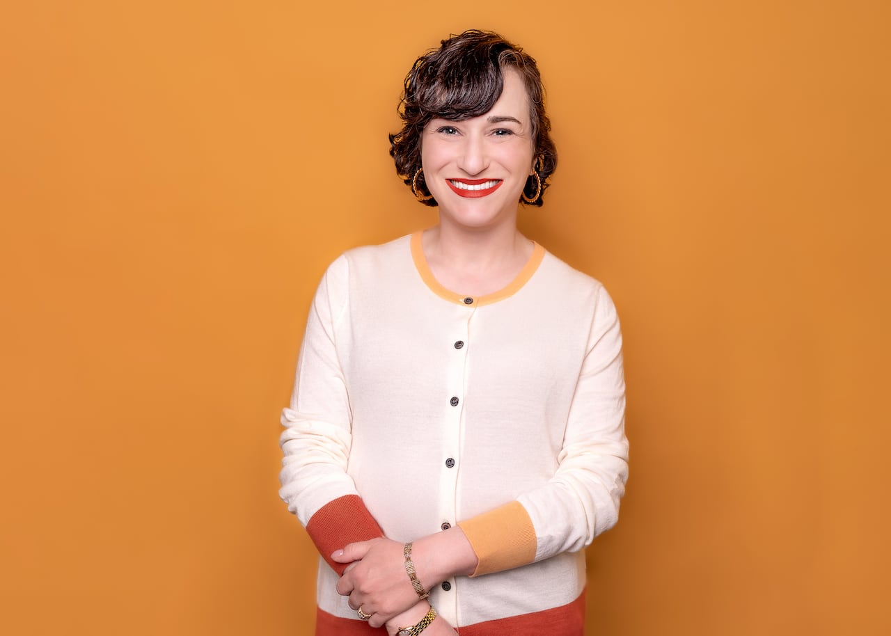 Sarina Isenberg, wearing a white sweater, smiles in front of a yellow background