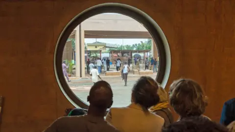 AFP/Getty Images Guests look out of a window as protesters storm the Museum of West African Art in Benin City - 9 November 2025