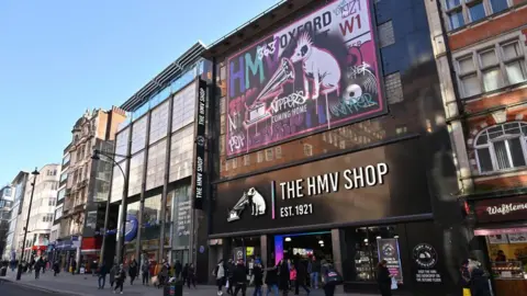 Getty Images A large music retail shop, the HMV shop. It has a logo of a white dog listening to a gramophone. There are lots of people walking across the shop on a busy street in London.