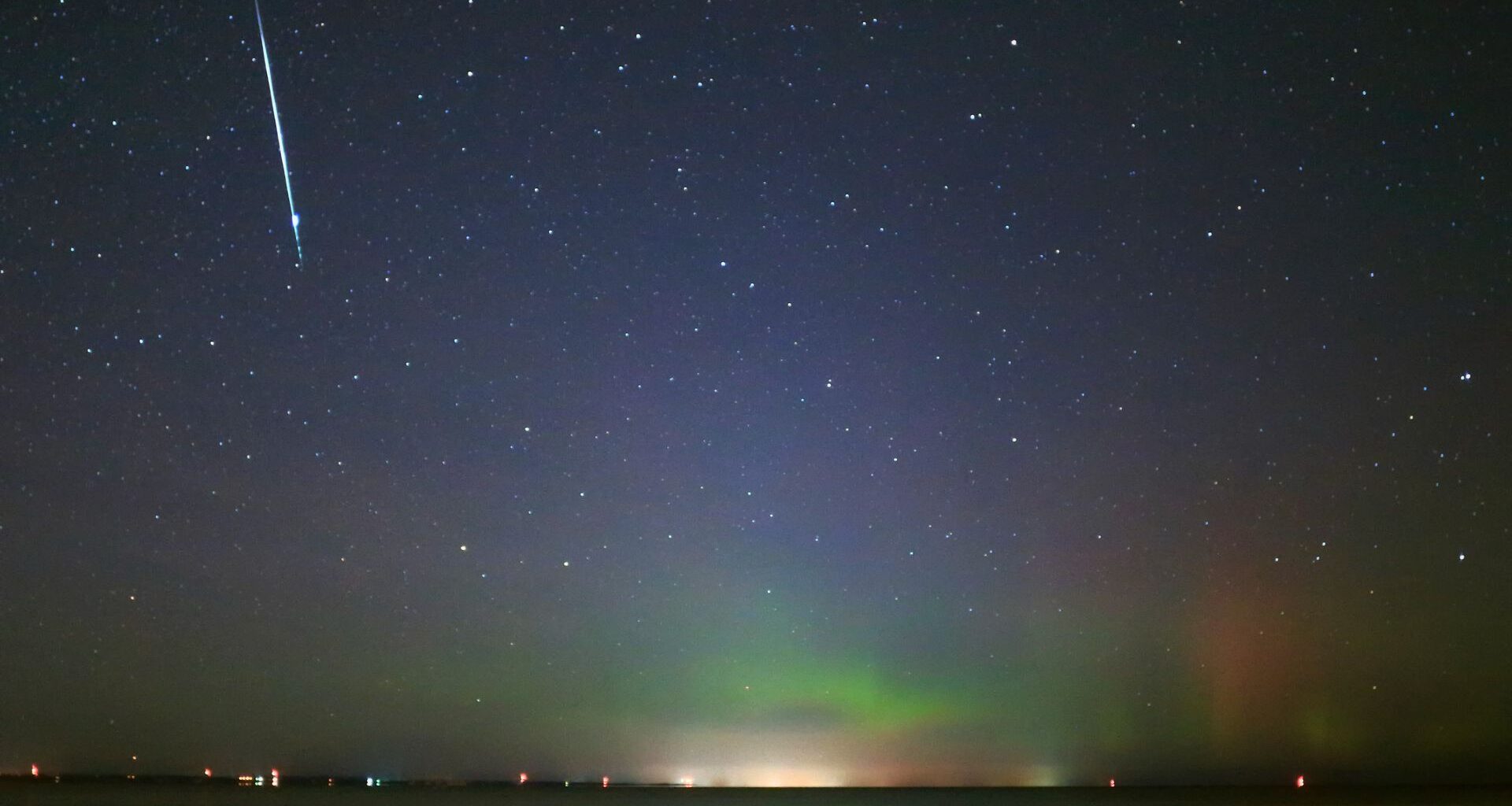 A streak of white light from a meteor graces the top left image of a blue and green starry night sky