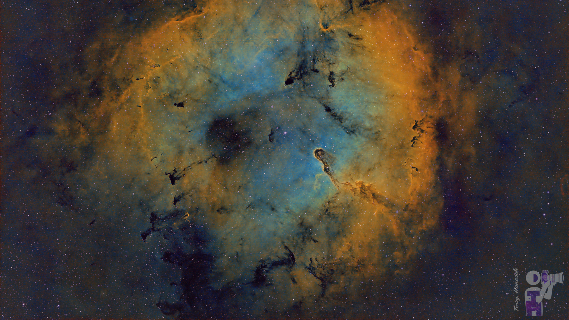 A colorful deep space nebula cloud dominates the center of an image, suspended against a distant starfield. The near-circular edge of the cloud is colored ochre, while the center is a pale blue. Dark twists of matter are also visible.