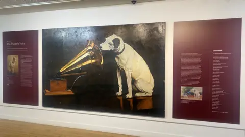Huguenot Museum A painting of a white dog with black ears listening into a Gramophone.  