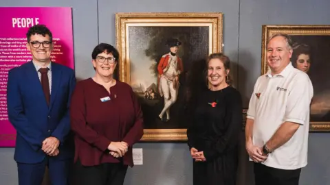 MNH Two men and two women smile and stand in front of the oil painting of Major Paul Crebbin.