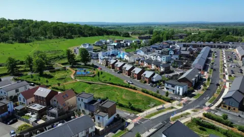 GHVDC An aerial shot of Graven Hill, with houses of different designs and shapes in the foreground, parks, and fields and forest in the background.