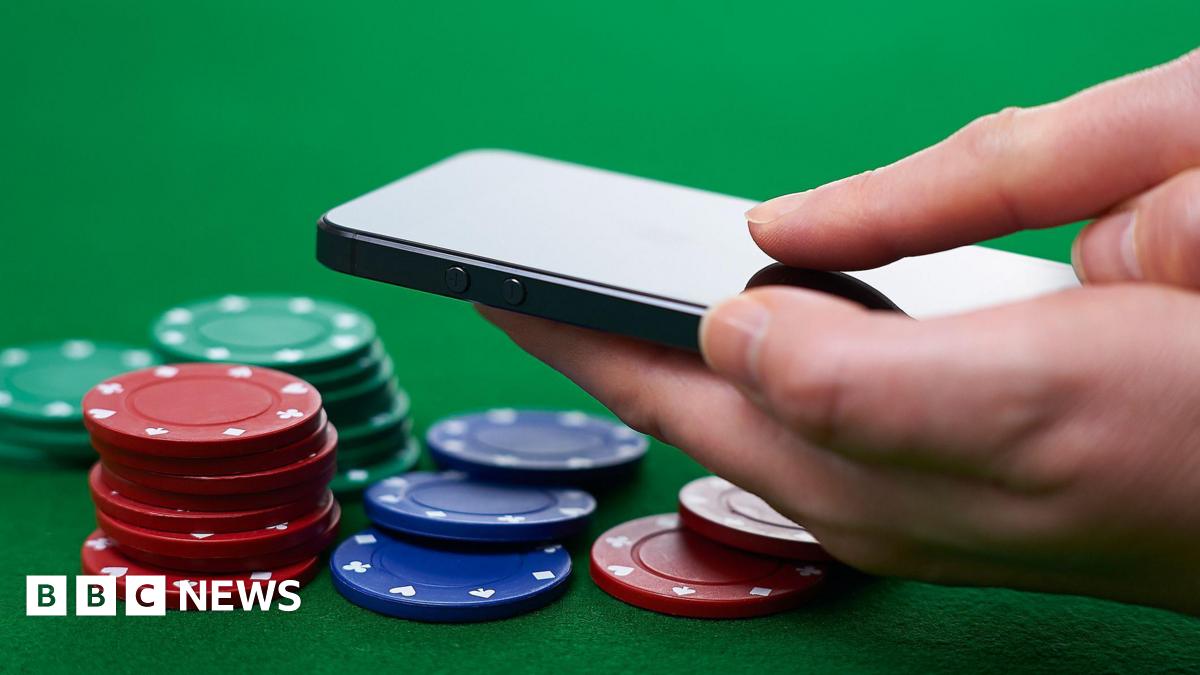 A hand holding a black smartphone, hovering over a selection of green, red and blue poker chips