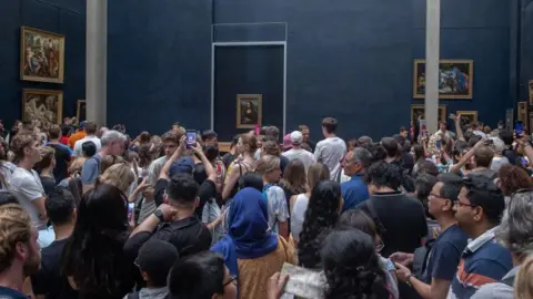 Getty Images A swarm of visitors take picture of the painting the Mona Lisa in a overcrowded gallery in the Louvre 
