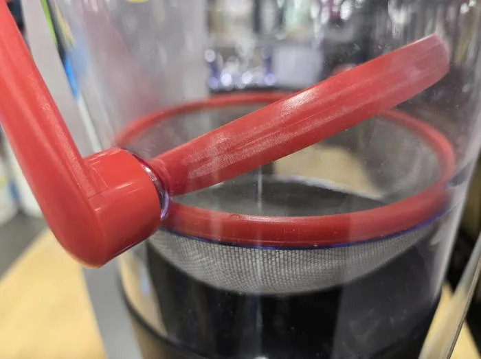 Close-up of a coffee press filter with red handle and mesh base, ready for brewing