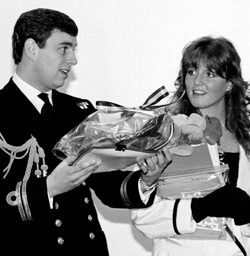 Prince Andrew wearing a naval uniform holding gifts smiling next to Sarah Ferguson .