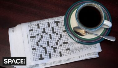 A black and white crossword puzzle sits underneath a blue and white coffee cup with the Space.com black and white logo in the bottom left corner.