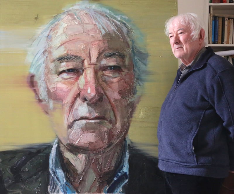 The late Seamus Heaney poses alongside Colin Davidson's portrait of him