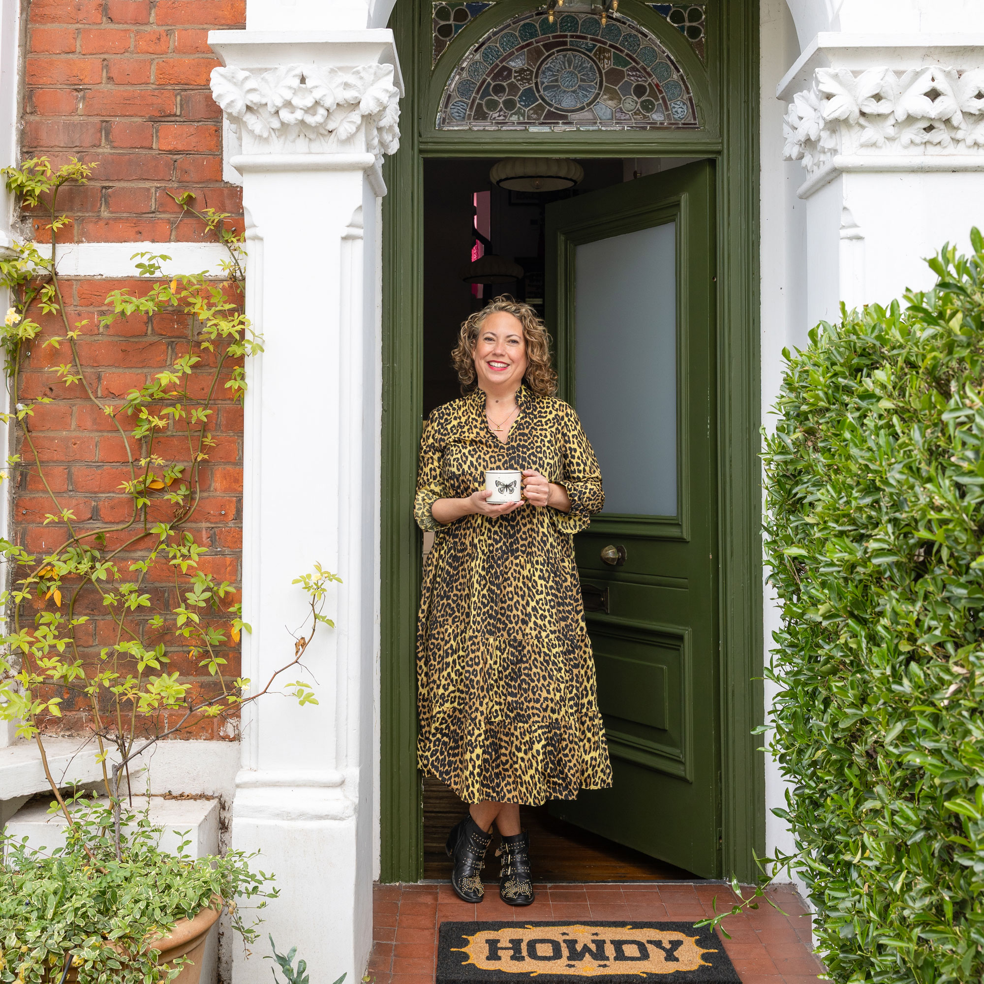 Front of house with olive green door and terracotta tiles with Lucy St George standing in the doorway